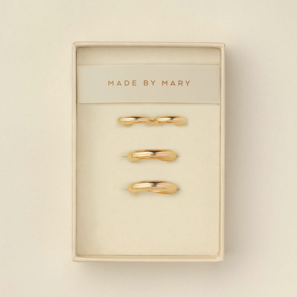 Two pairs of polished wide gold hoops, one smaller and one larger, displayed in a cream-colored presentation box with the brand name 'MADE BY MARY' printed on the insert.