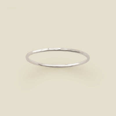 A thin silver hammered wire ring, shown on a solid light beige background.