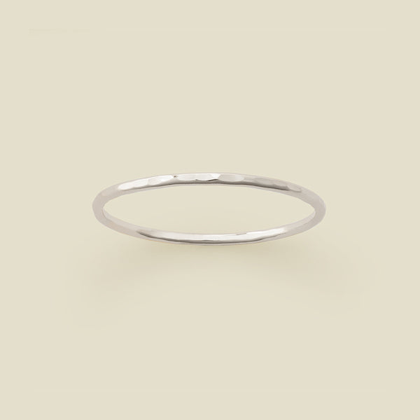 A thin silver hammered wire ring, shown on a solid light beige background.
