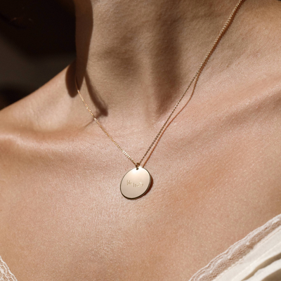 A lifestyle photo of a person's neck wearing a gold chain necklace with a round gold pendant engraved with handwritten script.