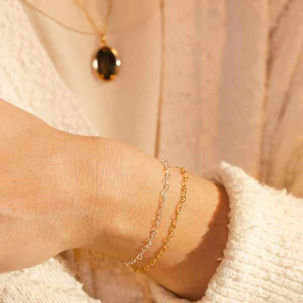 A person's wrist wearing a gold and silver heart link chain bracelet.