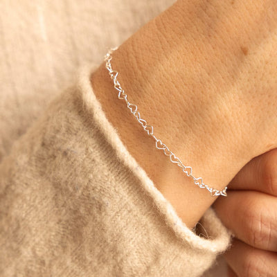 A person's wrist wearing a silver heart link chain bracelet.