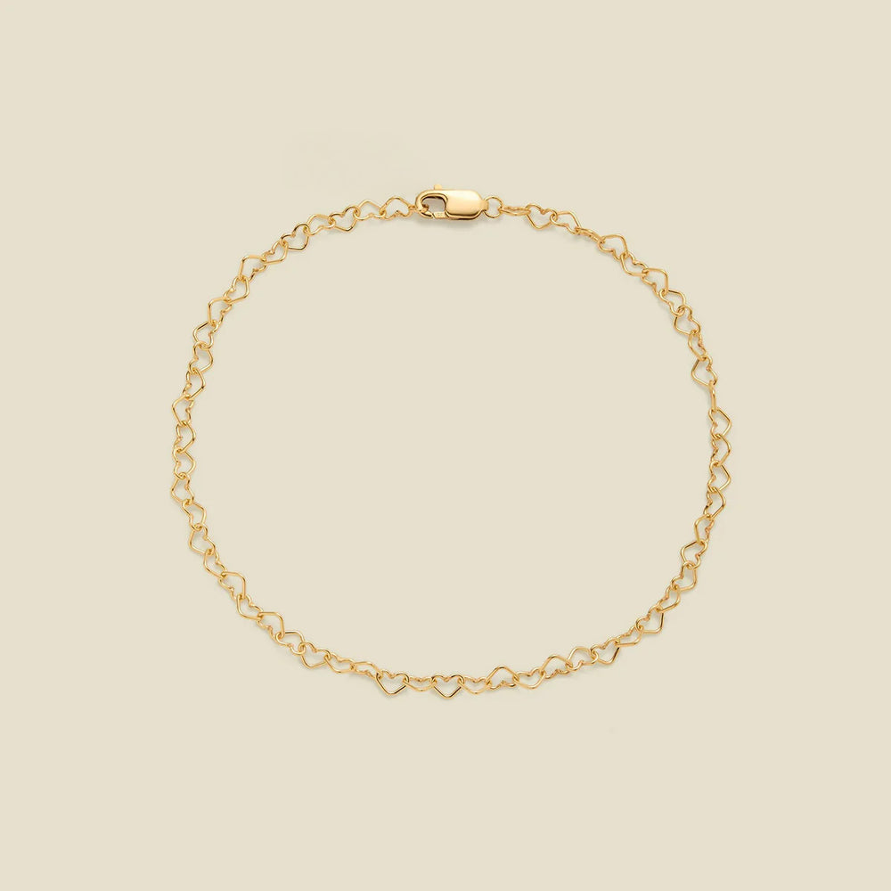 A delicate gold chain bracelet with a continuous open-heart link pattern and a lobster clasp, displayed on a solid light beige background.