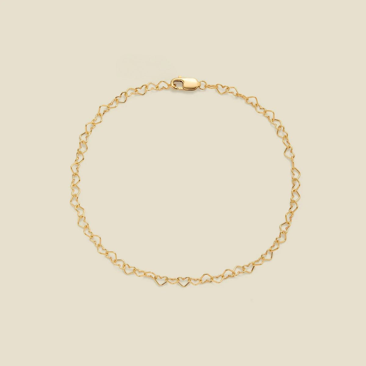 A delicate gold chain bracelet with a continuous open-heart link pattern and a lobster clasp, displayed on a solid light beige background.