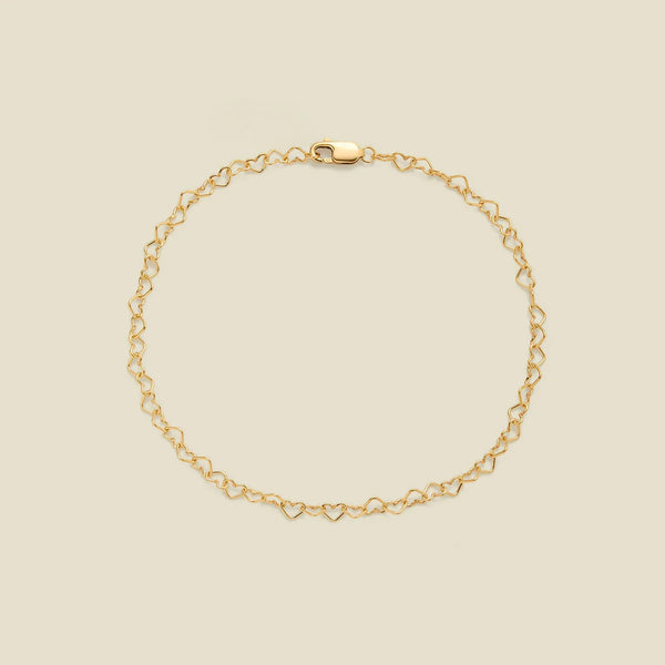 A delicate gold chain bracelet with a continuous open-heart link pattern and a lobster clasp, displayed on a solid light beige background.