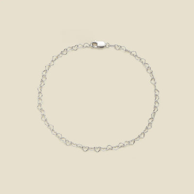 A delicate silver chain bracelet with a continuous open-heart link pattern and a lobster clasp, displayed on a solid light beige background.