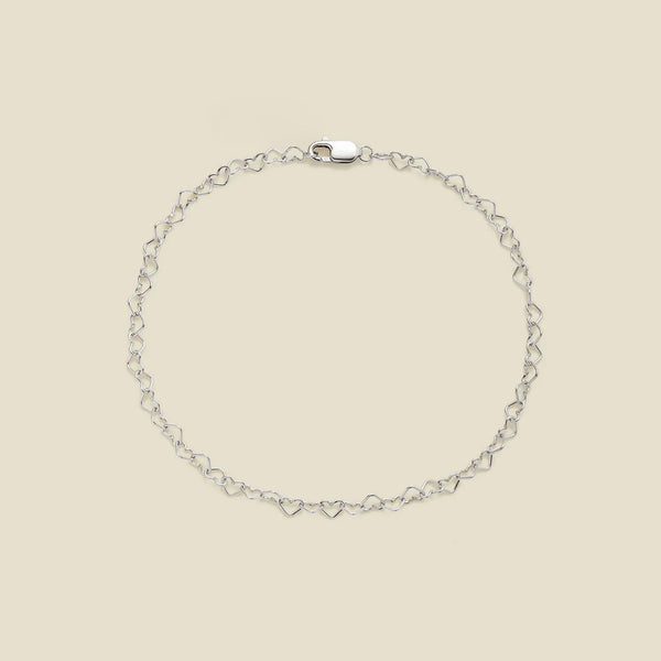 A delicate silver chain bracelet with a continuous open-heart link pattern and a lobster clasp, displayed on a solid light beige background.