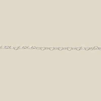 A silver heart link chain bracelet stretched horizontally across a solid light beige background.