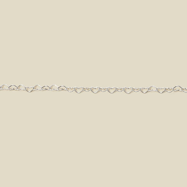A silver heart link chain bracelet stretched horizontally across a solid light beige background.