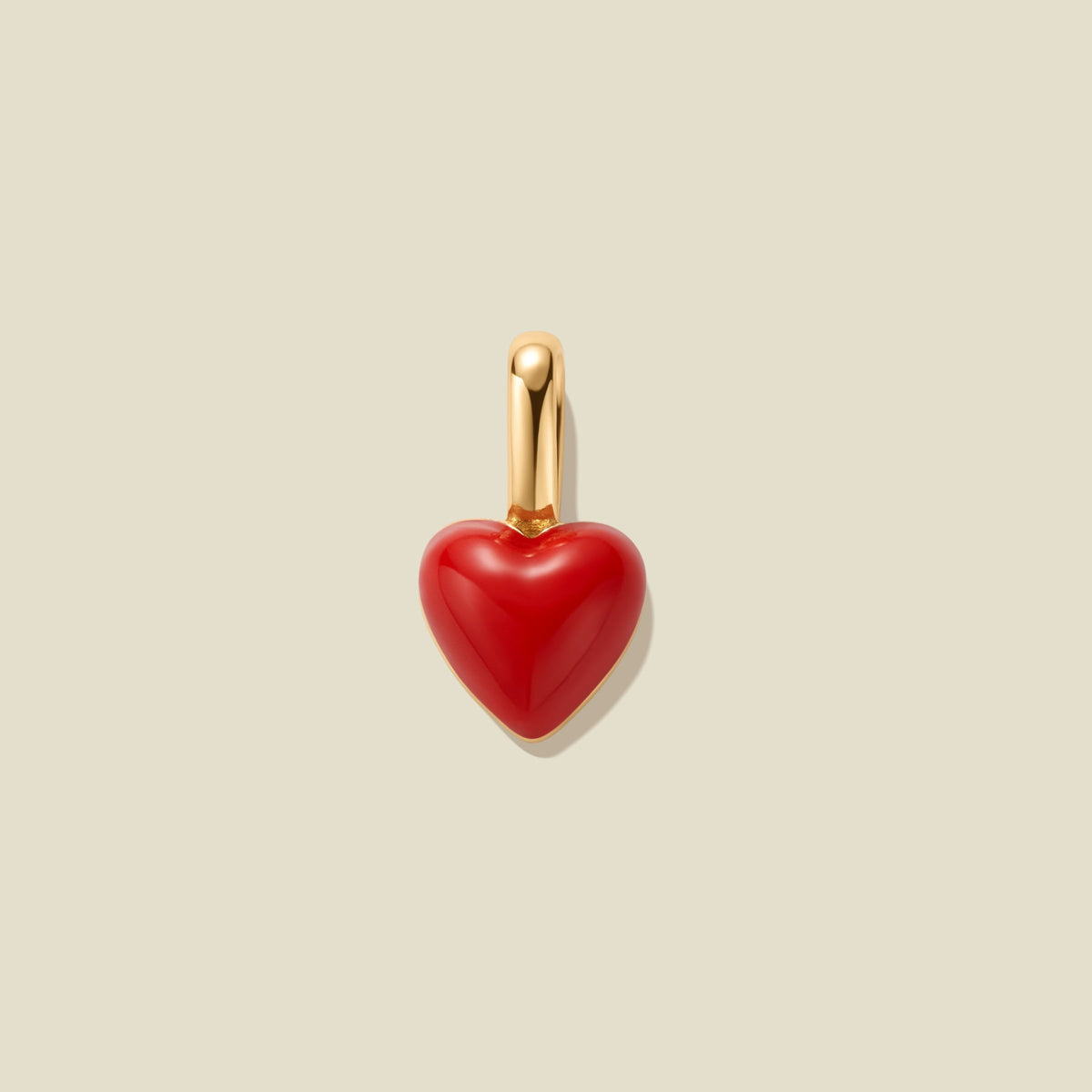 A small heart-shaped charm with a glossy red body and a polished gold bail, centered on a warm beige background.