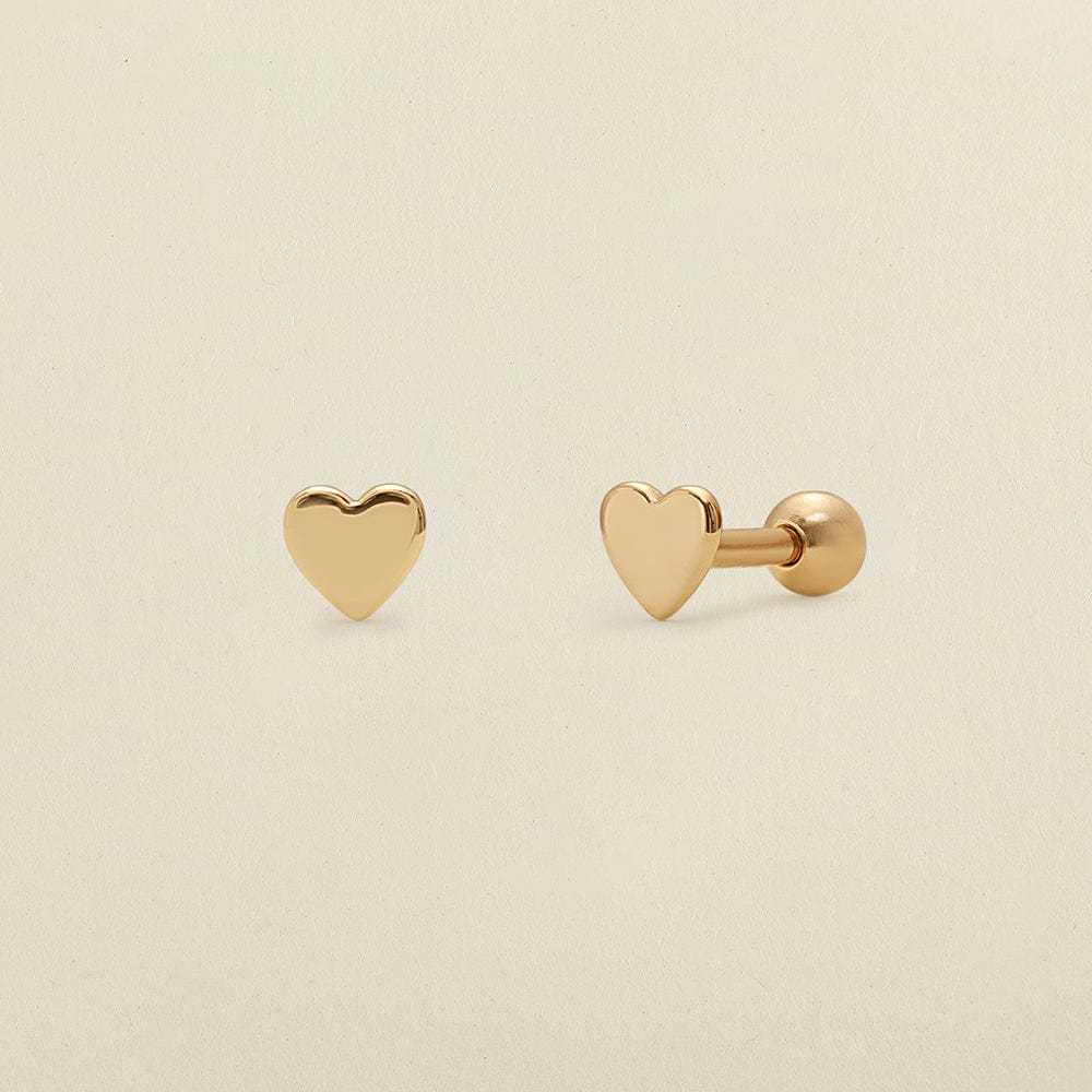 A pair of gold heart-shaped stud earrings, one shown from the front and the other from the side/back, on a light beige background.