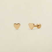 A pair of gold heart-shaped stud earrings, one shown from the front and the other from the side/back, on a light beige background.