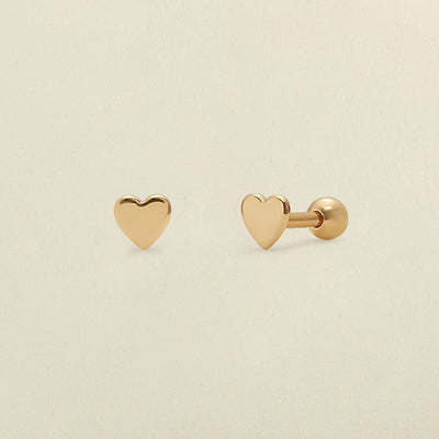 A pair of gold heart-shaped stud earrings, one shown from the front and the other from the side/back, on a light beige background.