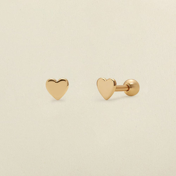 A pair of gold heart-shaped stud earrings, one shown from the front and the other from the side/back, on a light beige background.