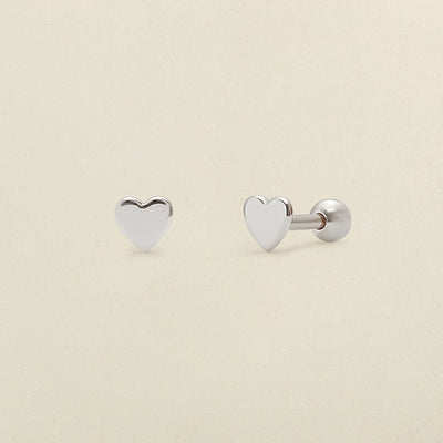 A pair of silver heart stud earrings with round ball backings, shown on a solid light beige background.