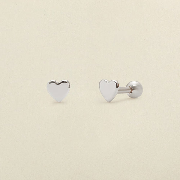 A pair of silver heart stud earrings with round ball backings, shown on a solid light beige background.