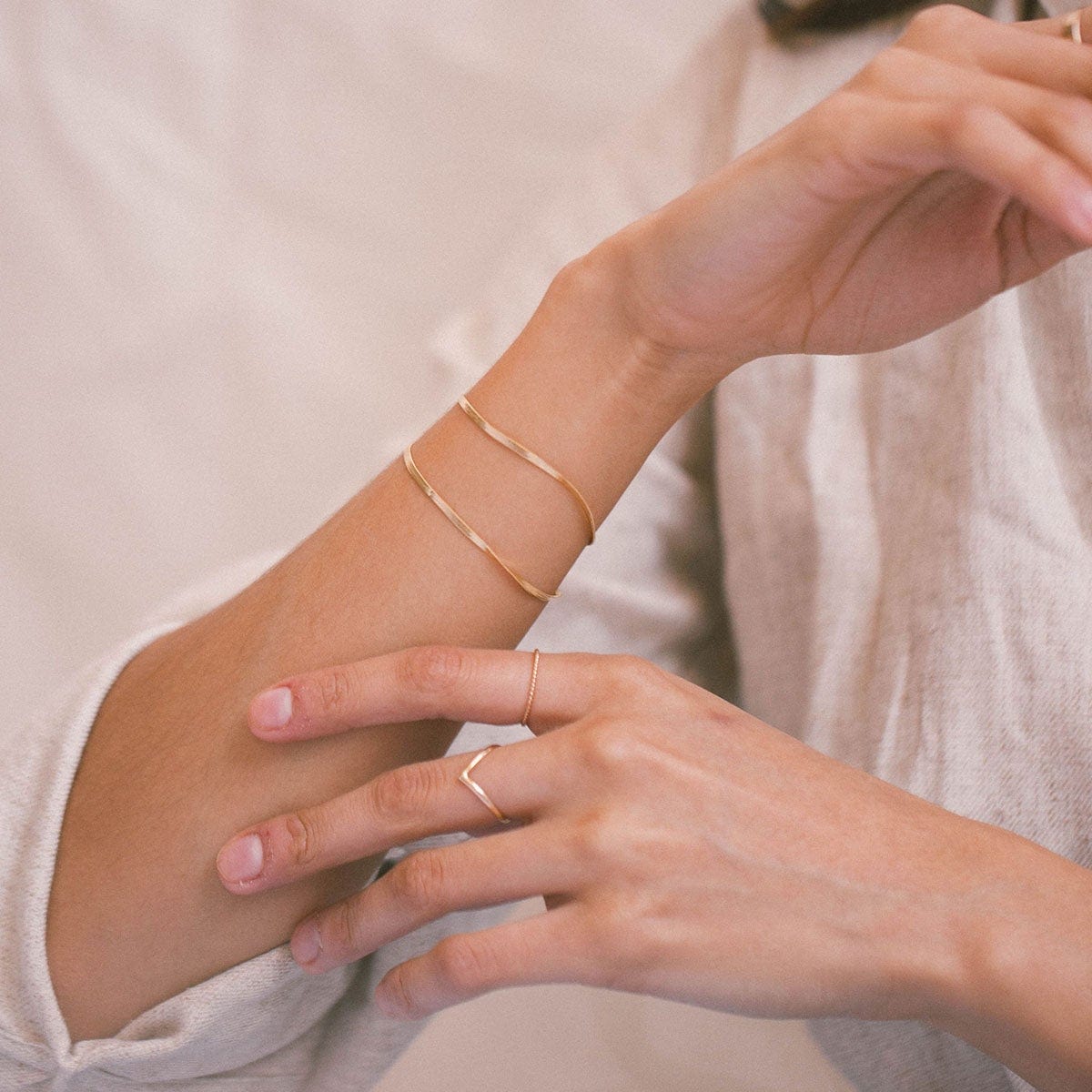 A woman's wrist wearing two thin gold bracelets.