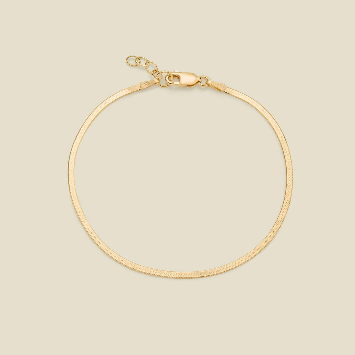 A gold flat wide bracelet with a lobster clasp, displayed on a solid light beige background.