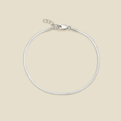 A silver flat wide bracelet with a lobster clasp, displayed on a solid light beige background.