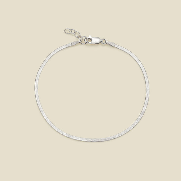 A silver flat wide bracelet with a lobster clasp, displayed on a solid light beige background.