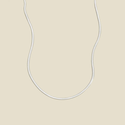 A silver flat wide necklace, displayed on a solid light beige background.