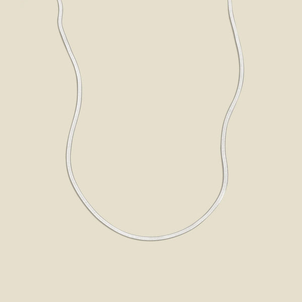 A silver flat wide necklace, displayed on a solid light beige background.