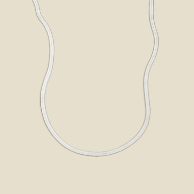 A silver flat wide necklace, displayed on a solid light beige background.