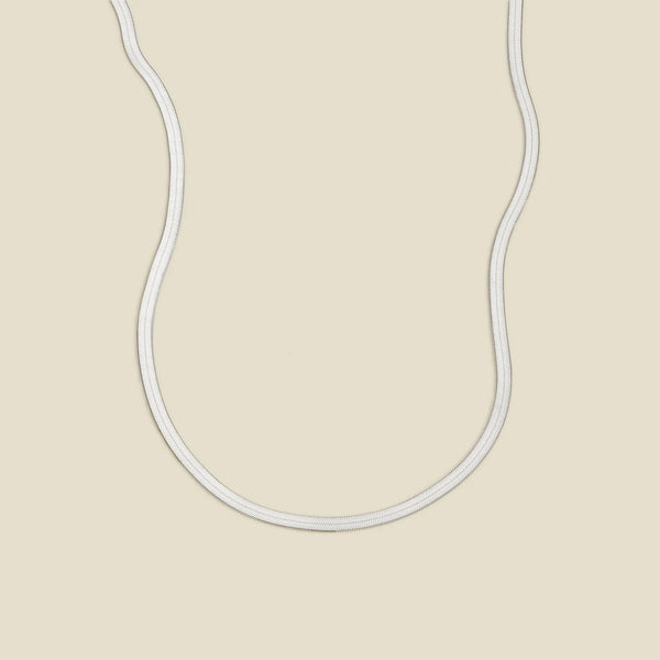 A silver flat wide necklace, displayed on a solid light beige background.