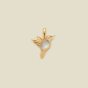 A gold bird charm with a smooth white stone belly and a small clear gemstone eye, centered on a solid beige background.