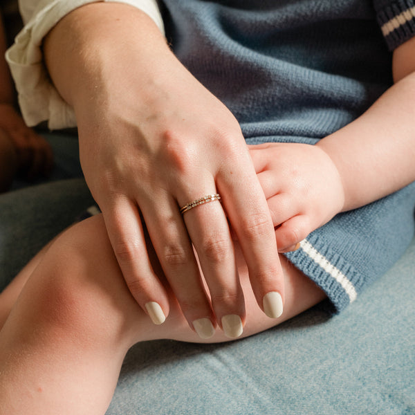 A hand resting on a small child's lap, showcasing two gold rings. Each ring has a different pattern of baguette and round cut clear gemstones.