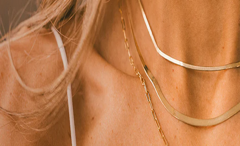 Close-up of a person wearing multiple layered gold necklaces with a neutral background