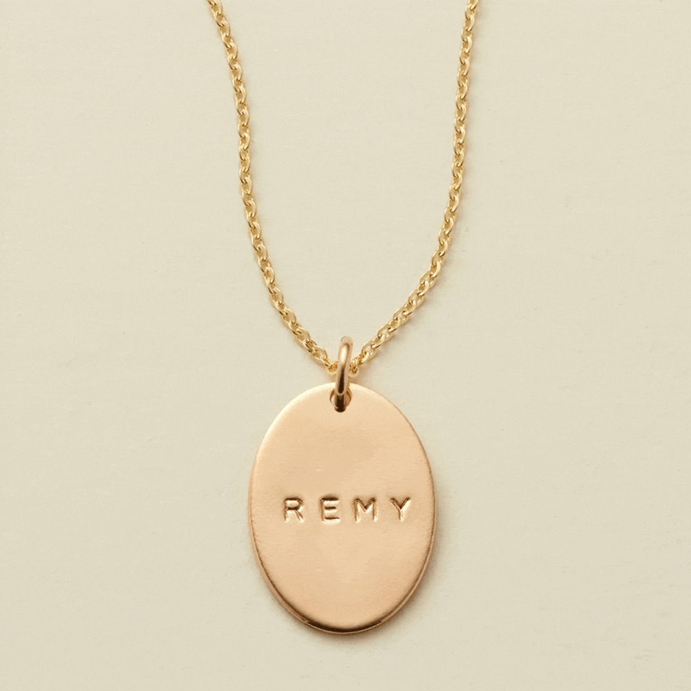 A gif of a delicate gold chain pendant necklace with a flat gold oval charm. The charm is engraved, and the engraving changes between different names.
