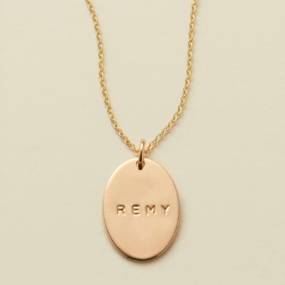 A gif of a delicate gold chain pendant necklace with a flat gold oval charm. The charm is engraved, and the engraving changes between different names.