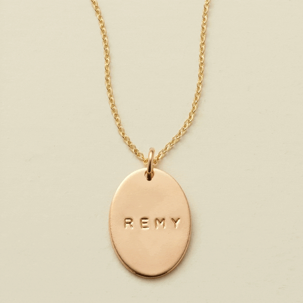 A gif of a delicate gold chain pendant necklace with a flat gold oval charm. The charm is engraved, and the engraving changes between different names.