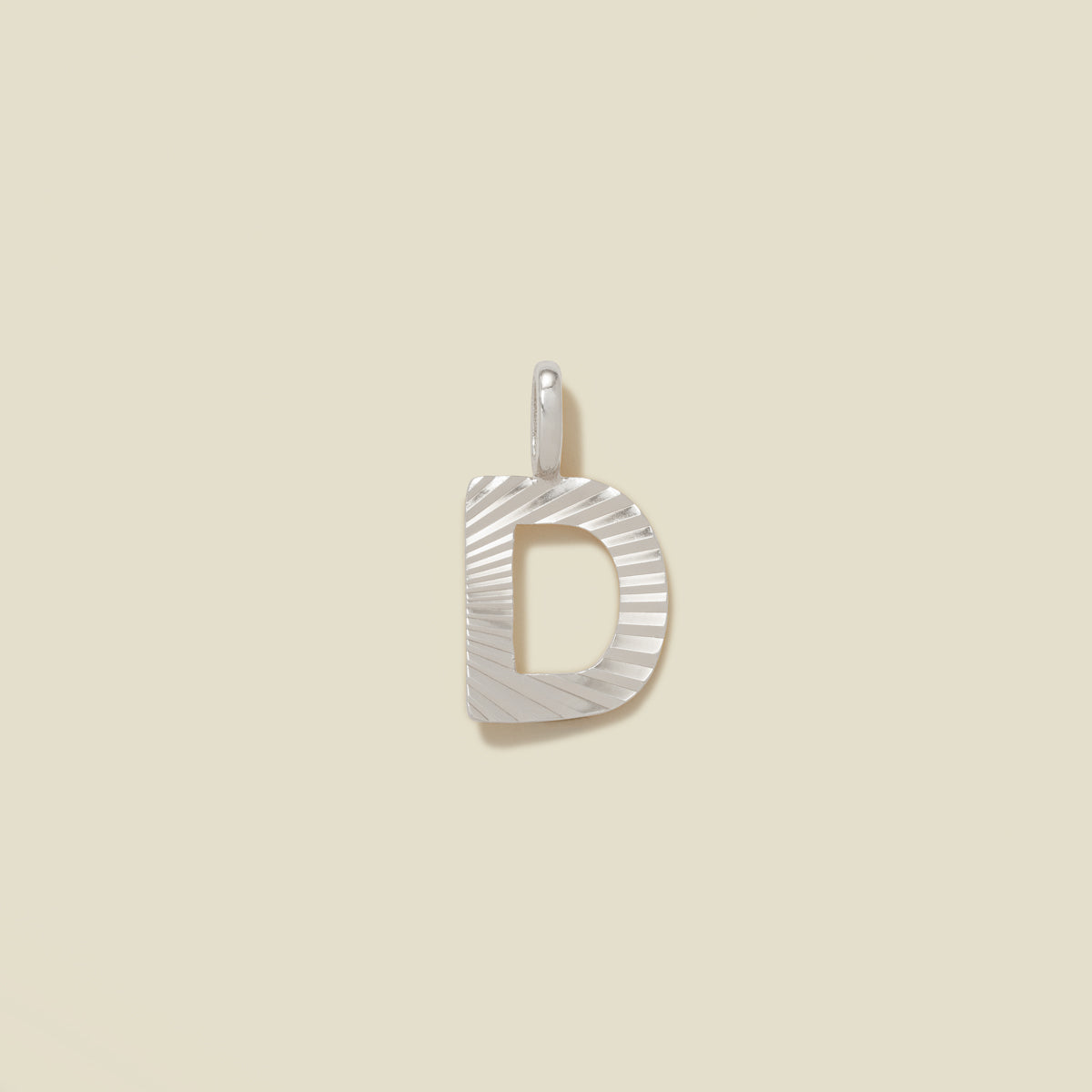 A small silver D-shaped charm with a textured, sunburst striped pattern, shown on a solid light beige background.