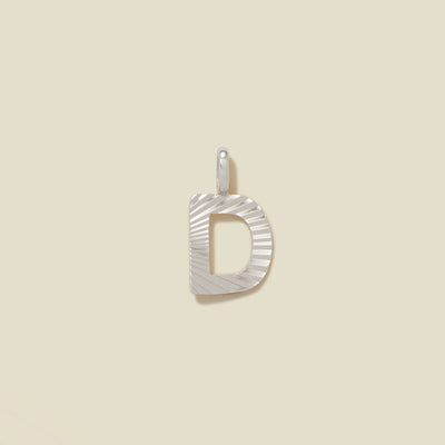 A small silver D-shaped charm with a textured, sunburst striped pattern, shown on a solid light beige background.