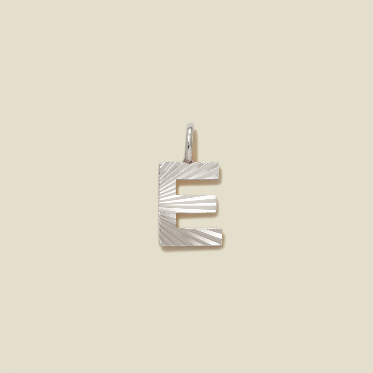 A small silver E-shaped charm with a textured, sunburst striped pattern, shown on a solid light beige background.