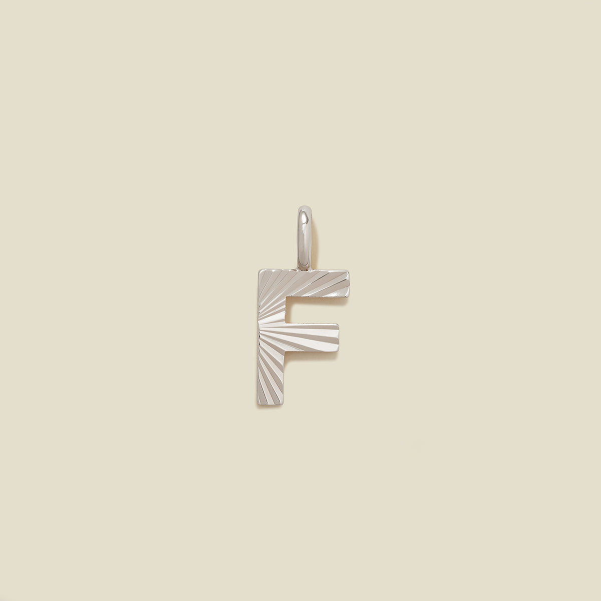 A small silver F-shaped charm with a textured, sunburst striped pattern, shown on a solid light beige background.