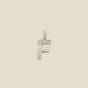 A small silver F-shaped charm with a textured, sunburst striped pattern, shown on a solid light beige background.