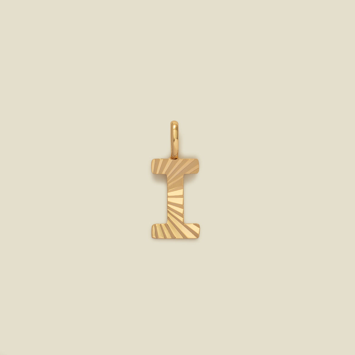 A small gold I-shaped charm with a textured, sunburst striped pattern, shown on a solid light beige background.