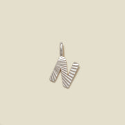 A small silver N-shaped charm with a textured, sunburst striped pattern, shown on a solid light beige background.