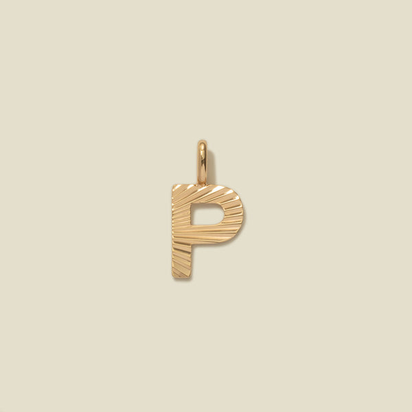 A small gold P-shaped charm with a textured, sunburst striped pattern, shown on a solid light beige background.