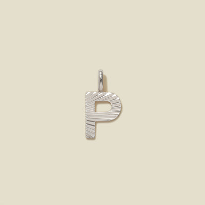A small silver P-shaped charm with a textured, sunburst striped pattern, shown on a solid light beige background.