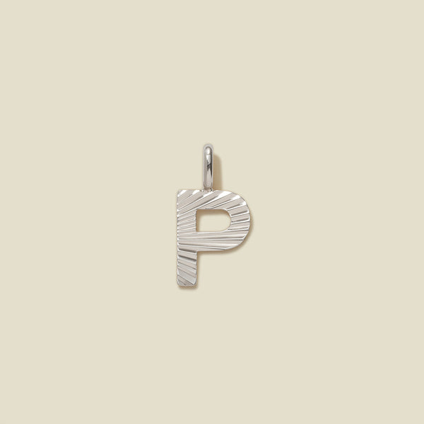 A small silver P-shaped charm with a textured, sunburst striped pattern, shown on a solid light beige background.