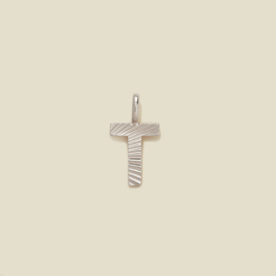 A small silver T-shaped charm with a textured, sunburst striped pattern, shown on a solid light beige background.