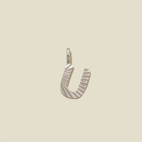 A small silver U-shaped charm with a textured, sunburst striped pattern, shown on a solid light beige background.