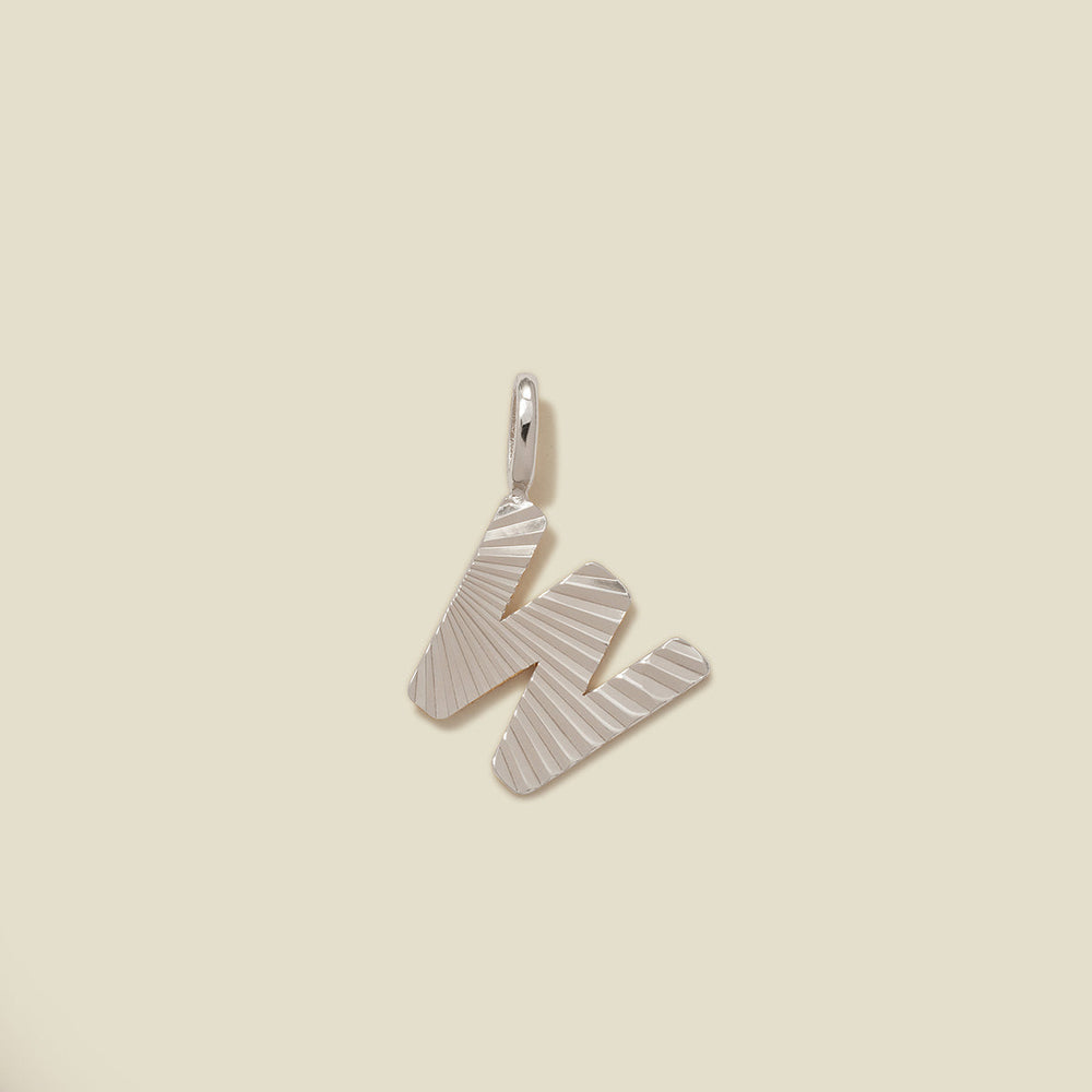A small silver W-shaped charm with a textured, sunburst striped pattern, shown on a solid light beige background.