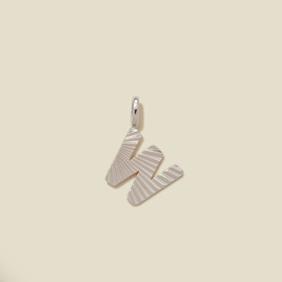 A small silver W-shaped charm with a textured, sunburst striped pattern, shown on a solid light beige background.