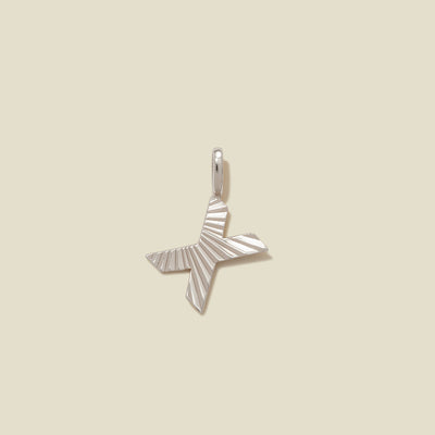 A small silver X-shaped charm with a textured, sunburst striped pattern, shown on a solid light beige background.