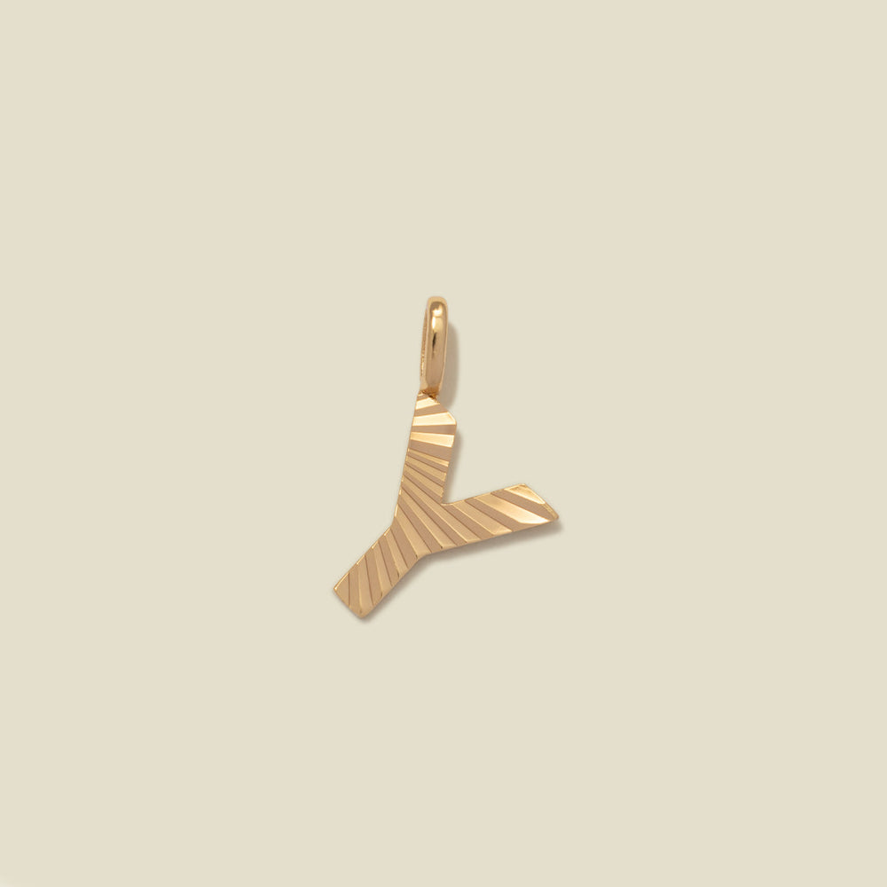 A small gold Y-shaped charm with a textured, sunburst striped pattern, shown on a solid light beige background.
